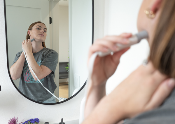 Woman looking in mirror using cleaning device.