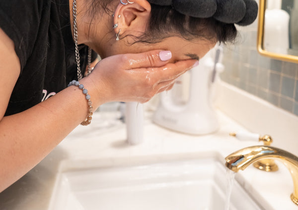 Woman with dark hair washing face at sink