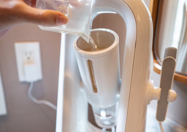 Hand with clear cup pouring liquid into device.